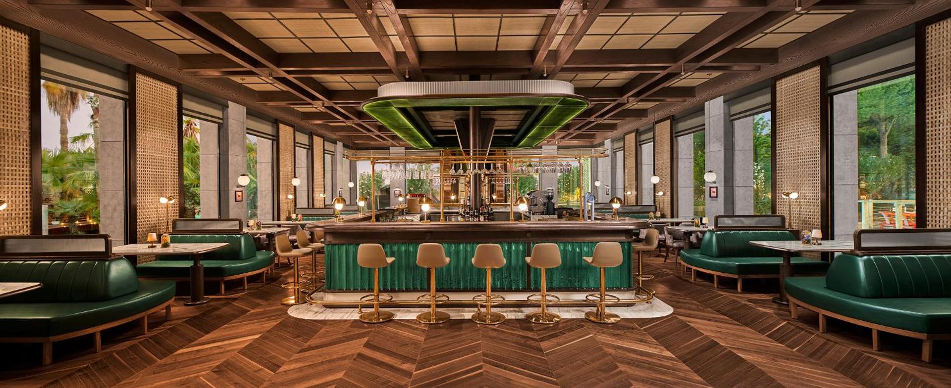 Gloria Serenity Resort elegants restorāns ar zaļiem dīvāniem, koka griestiem un centrālo bāru ar modernu apgaismojumu