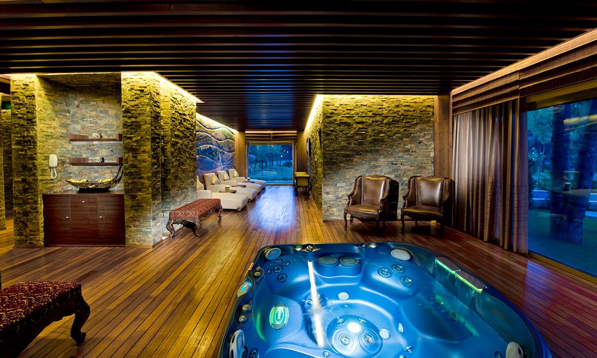Gloria Serenity Resort moderns spa atpūtas komplekss ar lielu džakuzi baseinu, akmens sienām un ērtiem atpūtas krēsliem