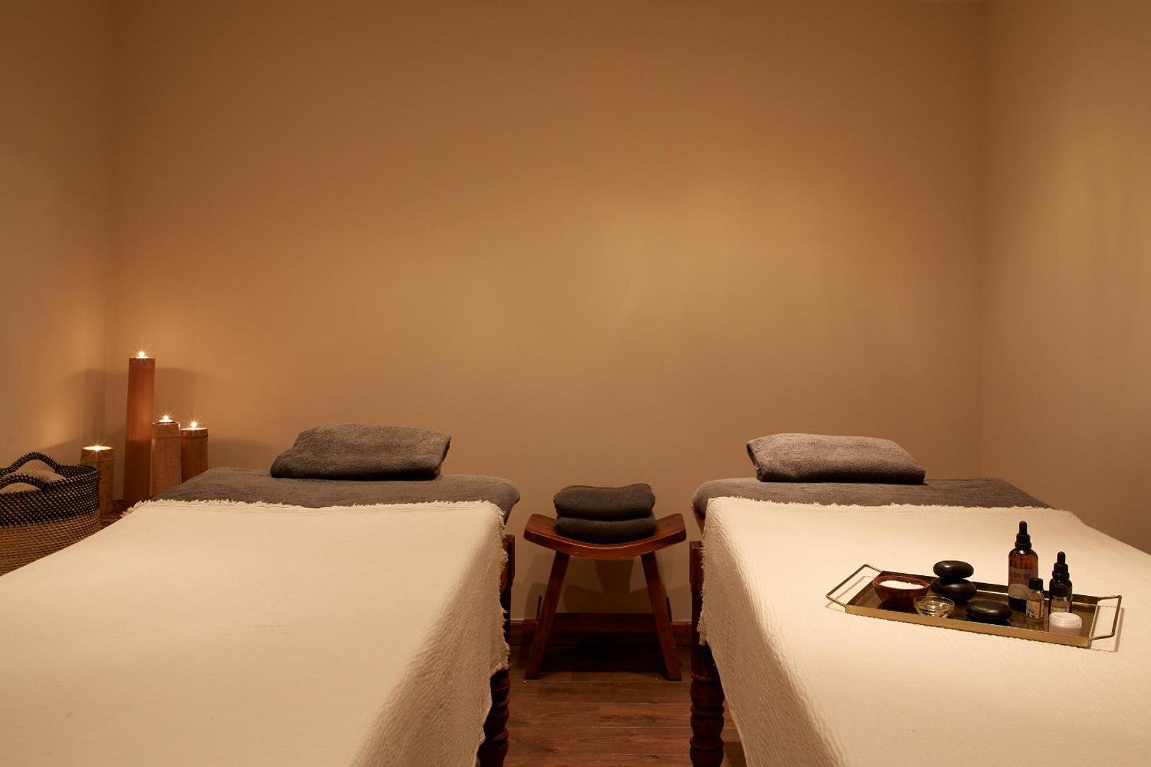Mājīga spa procedūru telpa viesnīcā Zeus Eleva Mirabello Bay ar divām masāžas gultām un siltu apgaismojumu romantiskai atpūtai.