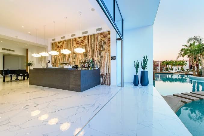 Stella Palace Aqua Park Resort modernais lobby bārs ar marmora grīdu un skatu uz āra baseinu un palmām saulrietā