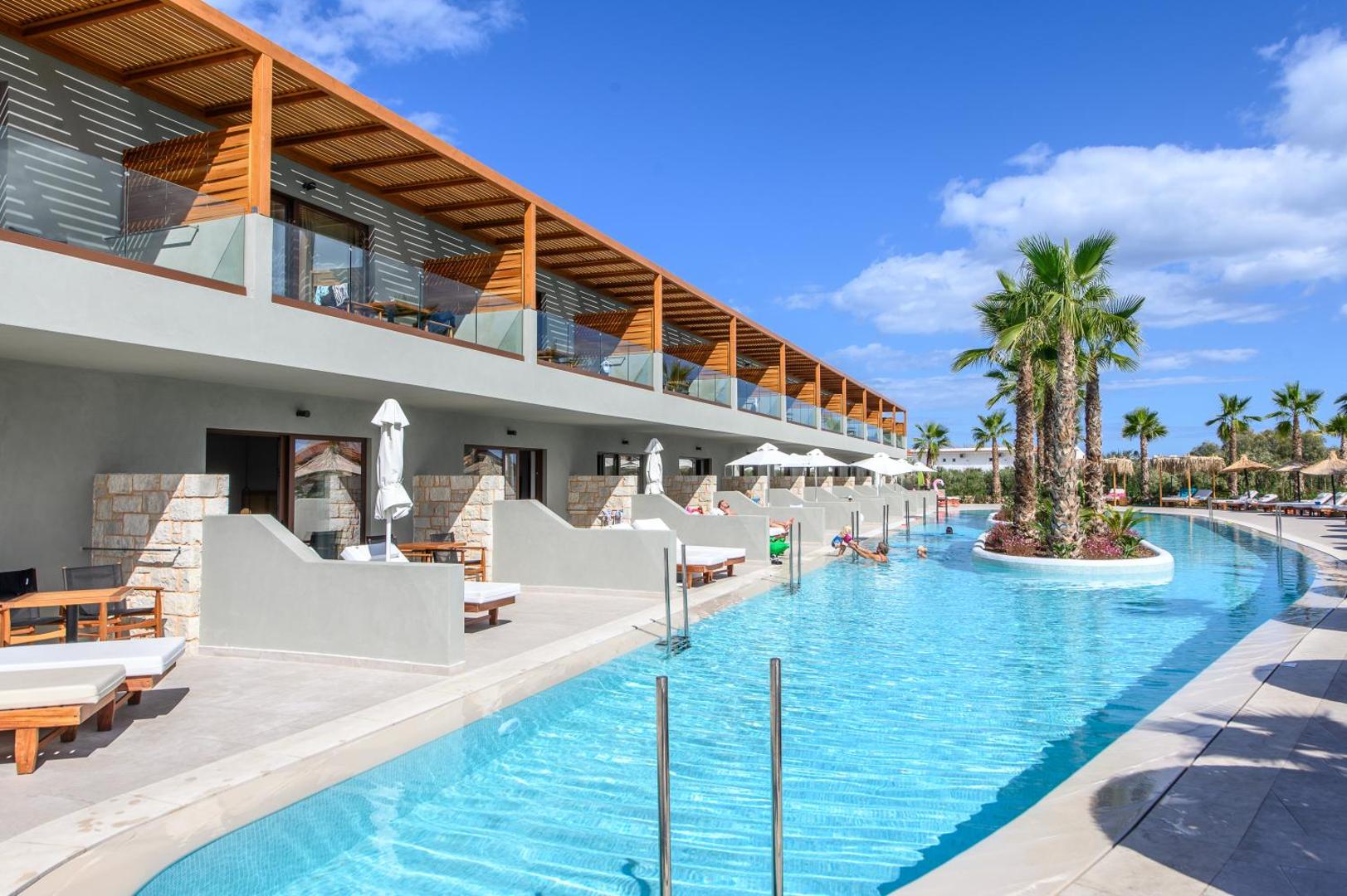 Stella Palace Aqua Park Resort koplietošanas baseins pie viesnīcas korpusa ar sauļošanās krēsliem un palmu salām