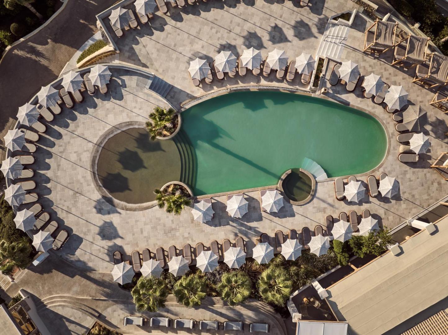 Seaside A Lifestyle Resort galvenā baseina skats no augšas Krētā — simetriski izvietoti saulessargi un sauļošanās krēsli ap gaiši zaļu baseinu