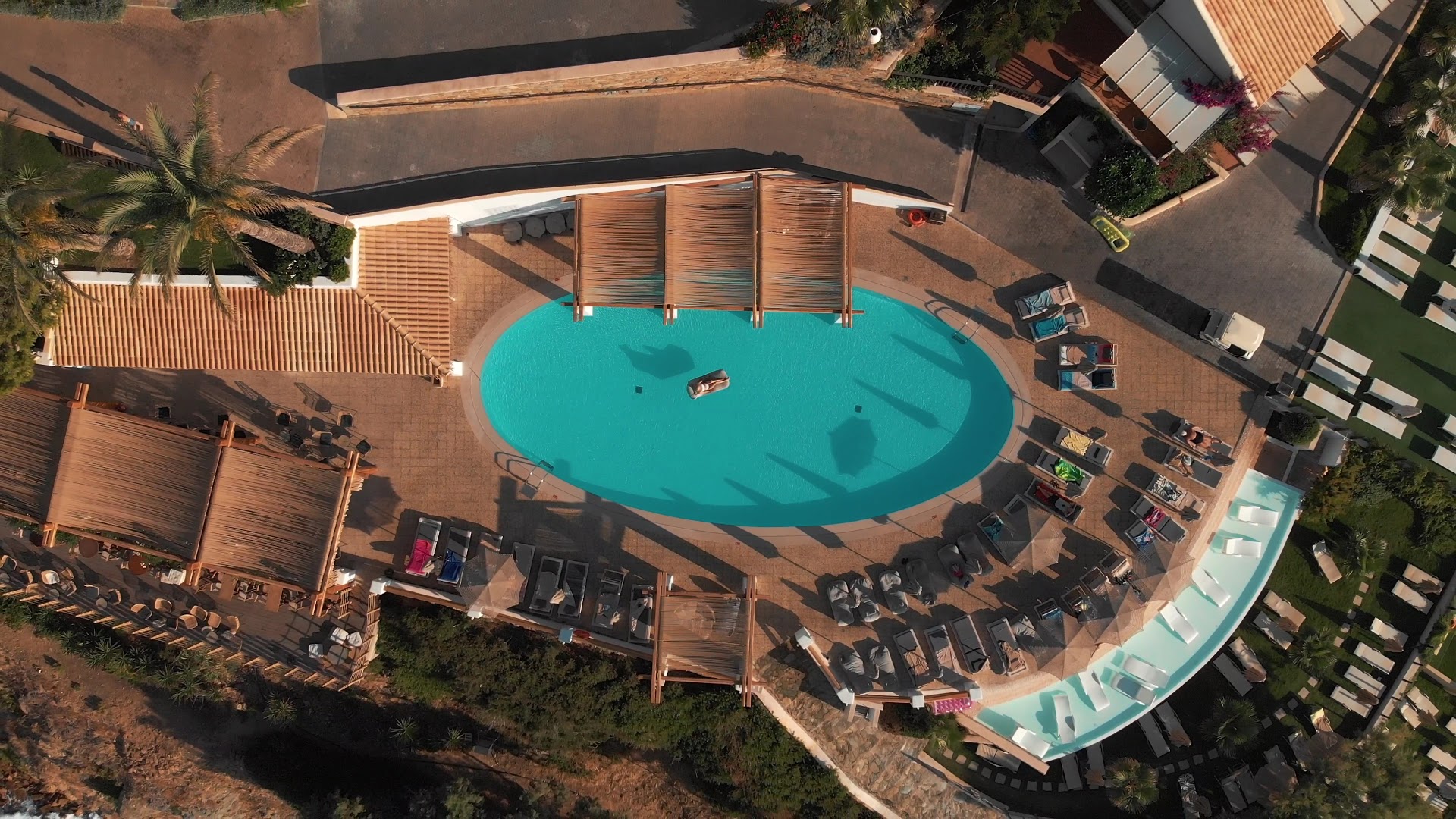 Seaside A Lifestyle Resort teritorijas aerofoto ar ovālu baseinu, terasēm un atpūtas zonām Krētas piekrastē saulrieta gaismā
