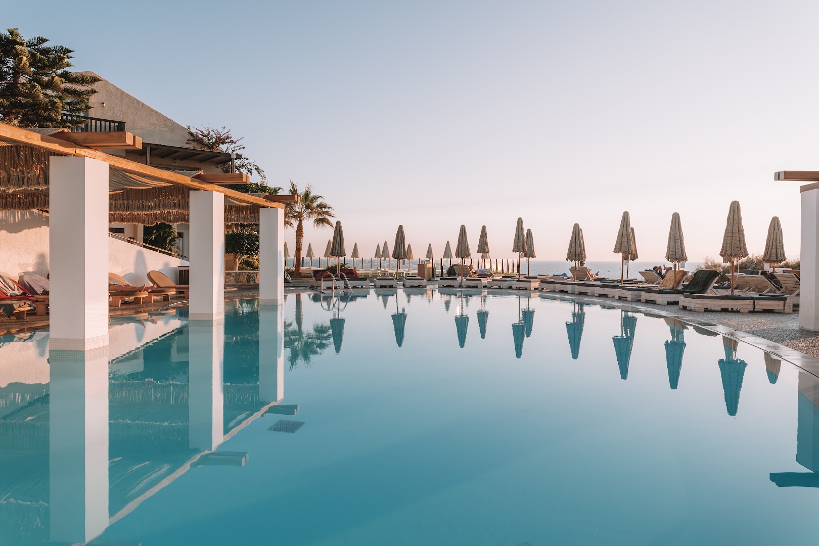 Seaside A Lifestyle Resort āra baseins rīta gaismā ar saulessargu atspulgu ūdenī un skatu uz jūru pie horizonta