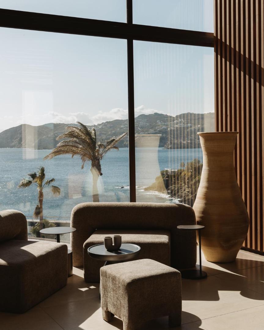 Skats no Seaside A Lifestyle Resort vestibila uz jūras līci un kalniem caur lielu panorāmas logu ar dizaina vāzi priekšplānā