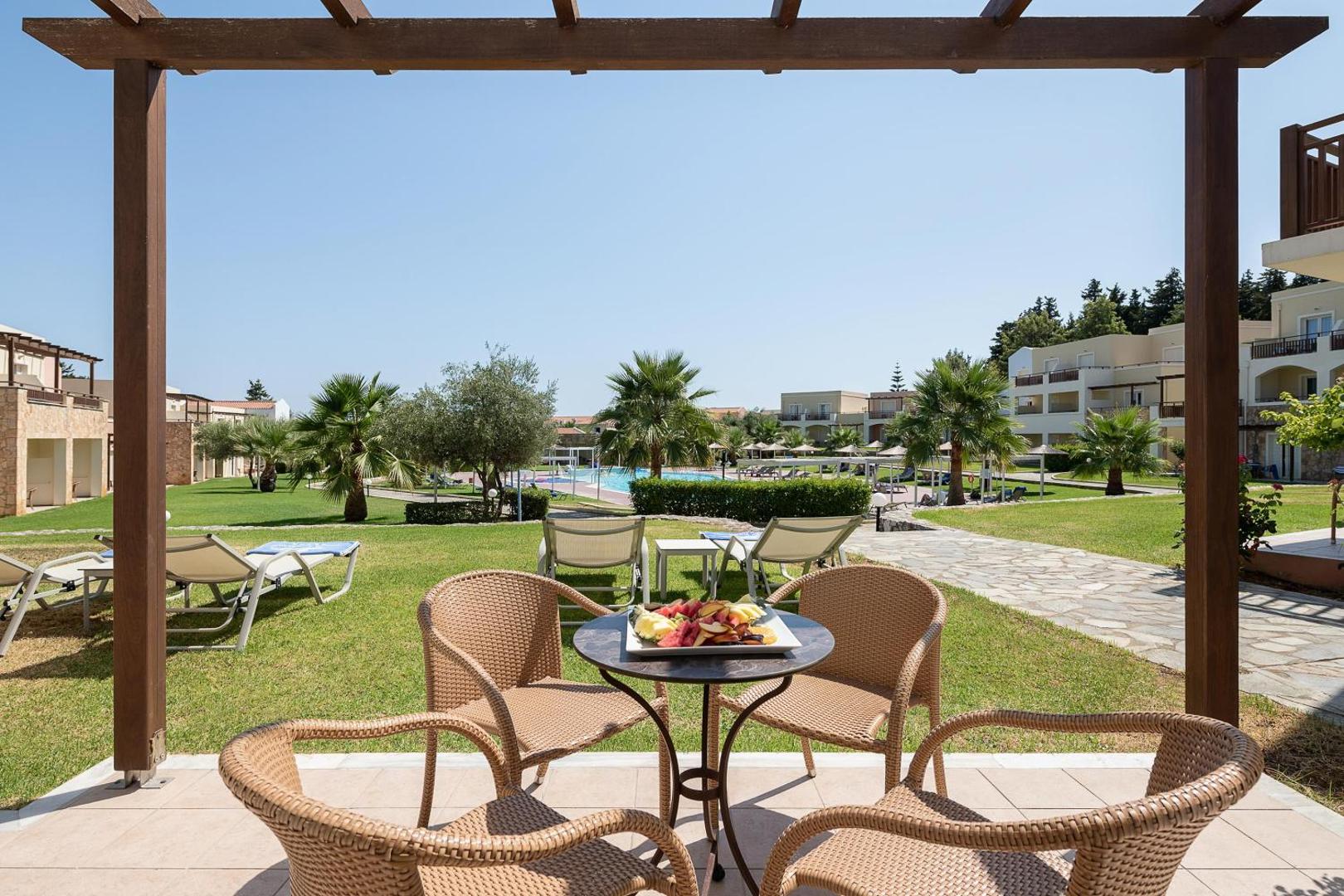 Pilot Beach Resort & Spa terase ar pītiem krēsliem un skatu uz viesnīcas dārzu, palmām un baseinu Georgiupoli