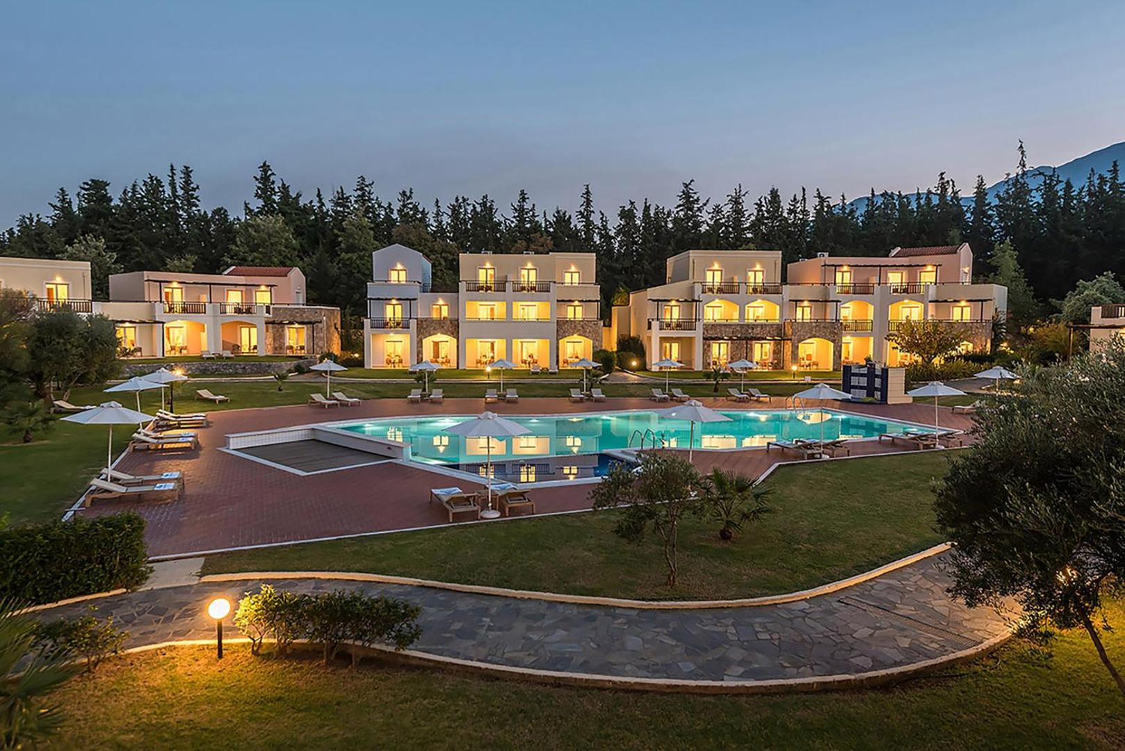 Pilot Beach Resort mājīgie divstāvu numuru korpusi vakarā ar izgaismotu baseinu, sauļošanās krēsliem un koptu dārzu