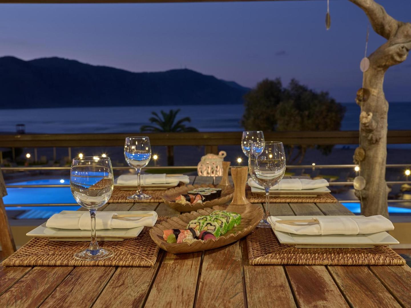 Pilot Beach Resort restorāna galdiņš ar suši izlasi saulrietā, skats uz jūru un baseinu Georgiupoles piekrastē, Krētā