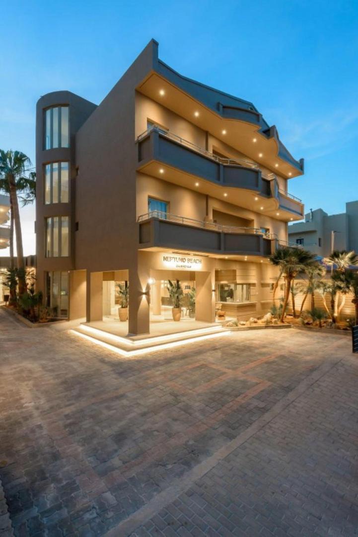 Zeus Hotels Neptuno Beach modernā fasāde un ieeja vakarā ar siltu apgaismojumu, palmām un bruģētu piebraucamo ceļu