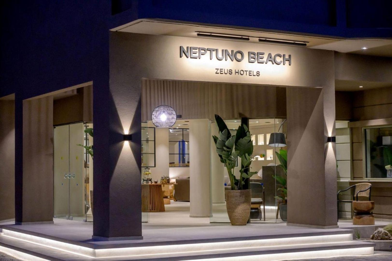 Neptuno Beach viesnīcas lobby ieeja ar izkārtni, dizaina gaismekļiem un dekoratīviem augiem podos vakara stundā