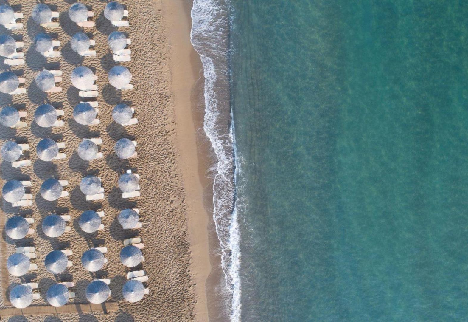 Zeus Hotels Neptuno Beach skats no putna lidojuma uz smilšu pludmali un dzidro jūras ūdeni Amudarā, Krētā ar saulessargiem