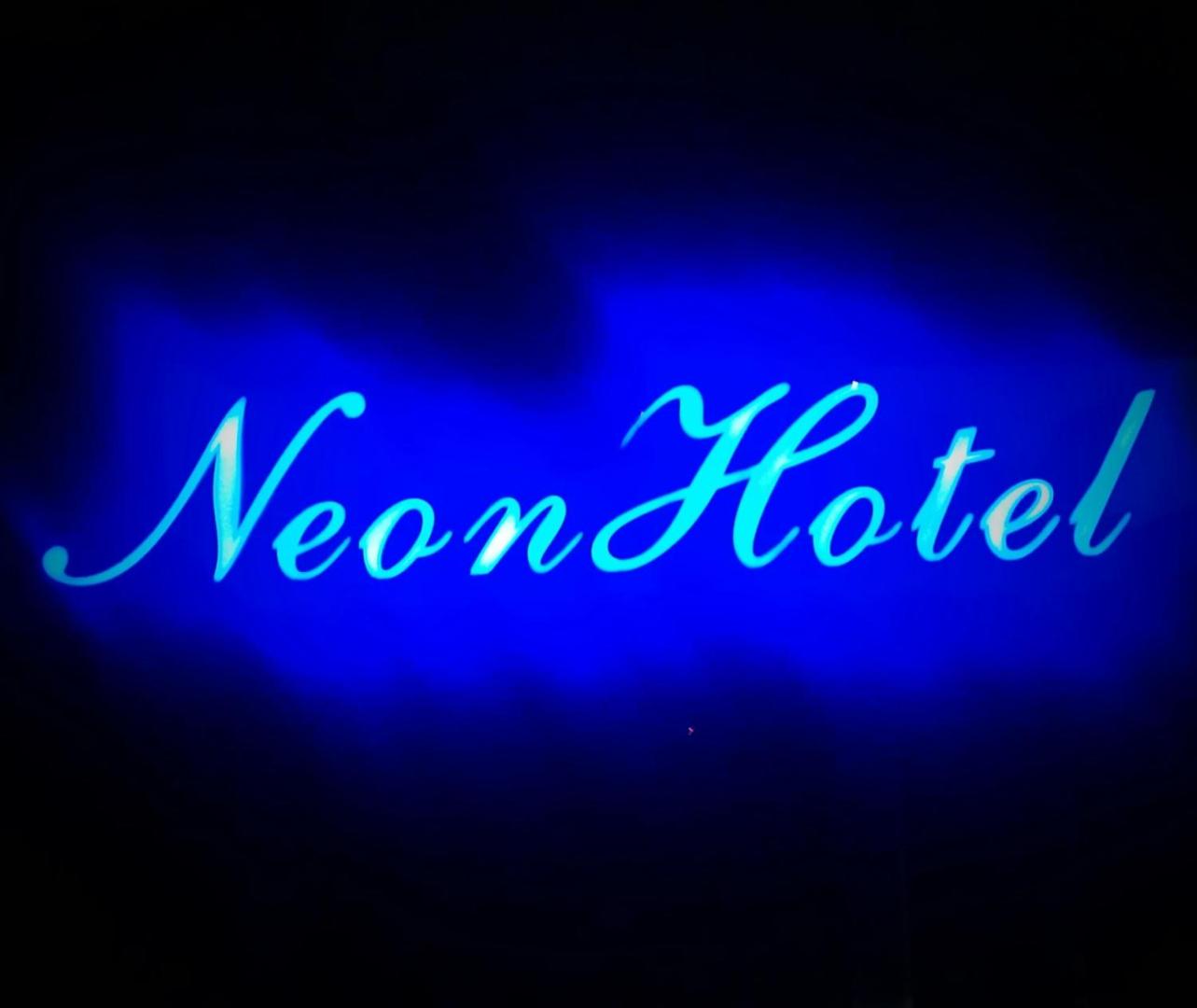 Neon Hotel zila neona izkārtne uz tumša fona — viesnīcas zīmola vizuālais noformējums nakts laikā