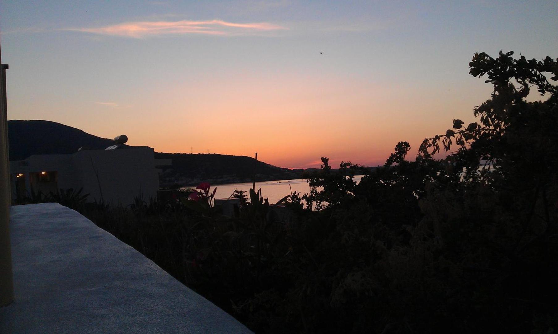 Panorāmas skats no Neon Hotel terases uz Stalidas līci un kalniem saulrieta gaismā, apkārtnē zaļojoši augi
