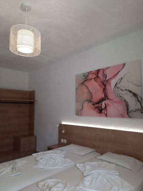 Neon Hotel numura detaļas ar mākslas darbu pie sienas, modernu lampu un koka mēbelēm gaišos toņos