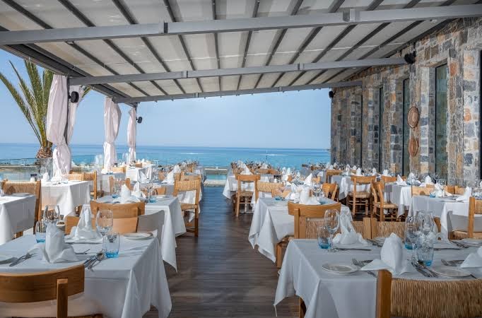 Nana Golden Beach āra terases restorāns ar balti klātiem galdiem zem nojumes un skatu uz zilo jūru
