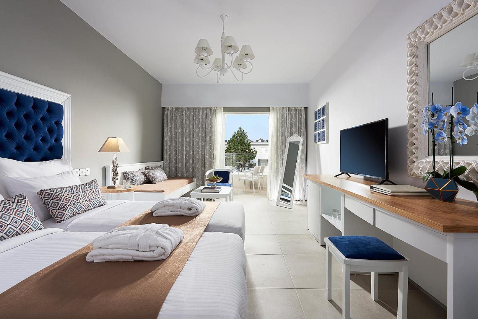 Gaišs un mūsdienīgs Mythos Palace Resort & Spa viesnīcas numurs ar ziliem akcentiem, balkonu un skatu uz dārzu