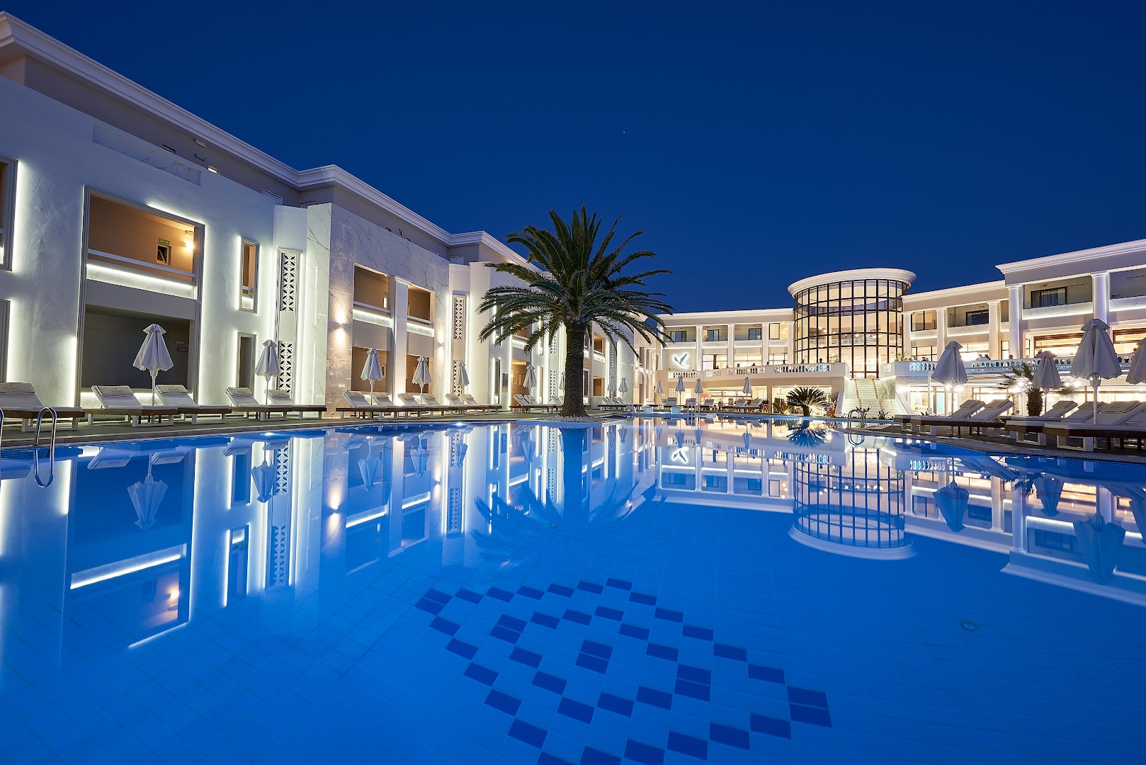 Viesnīcas Mythos Palace Resort & Spa nakts skats uz baseinu un arhitektūru ar spoguļattēlu ūdenī un vakara apgaismojumu