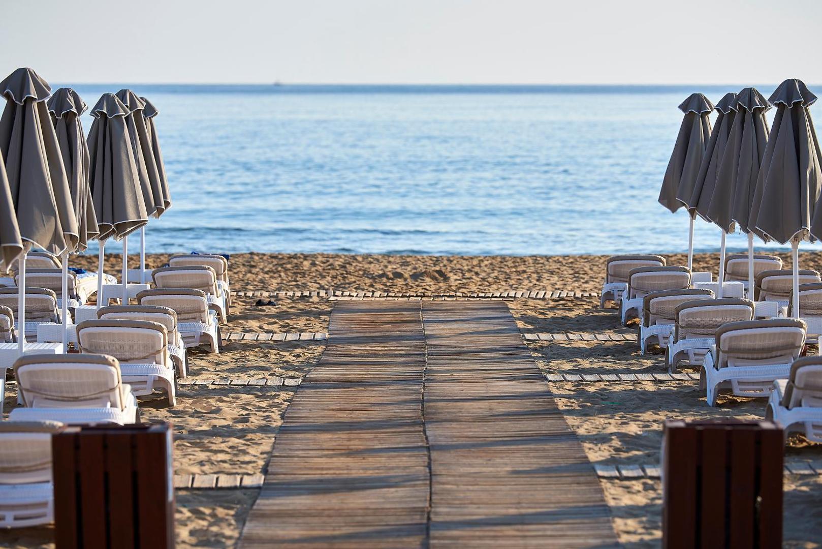 Mythos Palace Resort & Spa privātā smilšu pludmale ar sauļošanās krēsliem, saulessargiem un koka laipu uz jūru