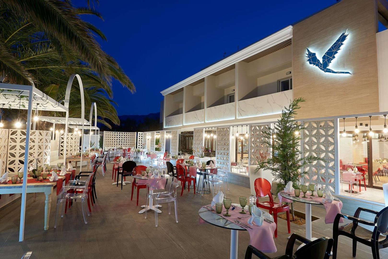Mythos Palace Resort & Spa āra terases restorāns vakarā ar modernām mēbelēm un izgaismotu viesnīcas fasādi Georgiupoli, Krētā
