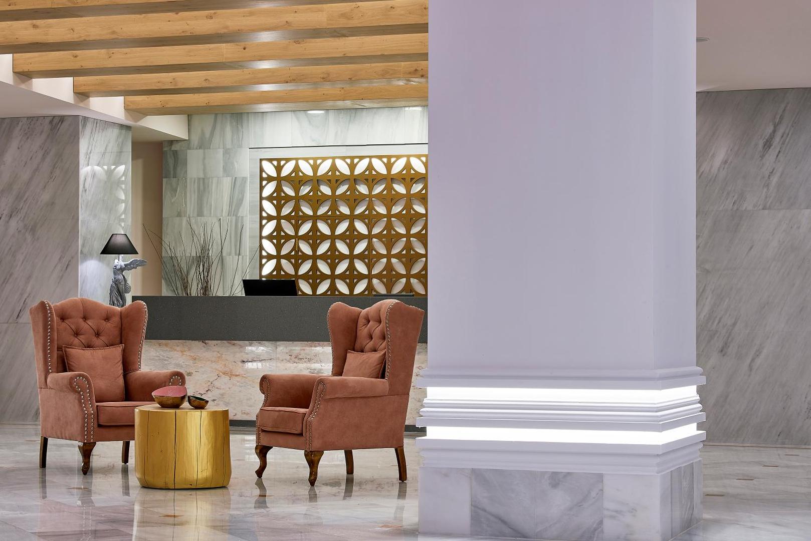 Mythos Palace Resort & Spa eleganta lobby zona ar marmora apdari, moderniem atpūtas krēsliem un viesmīlīgu recepcijas galdiņu