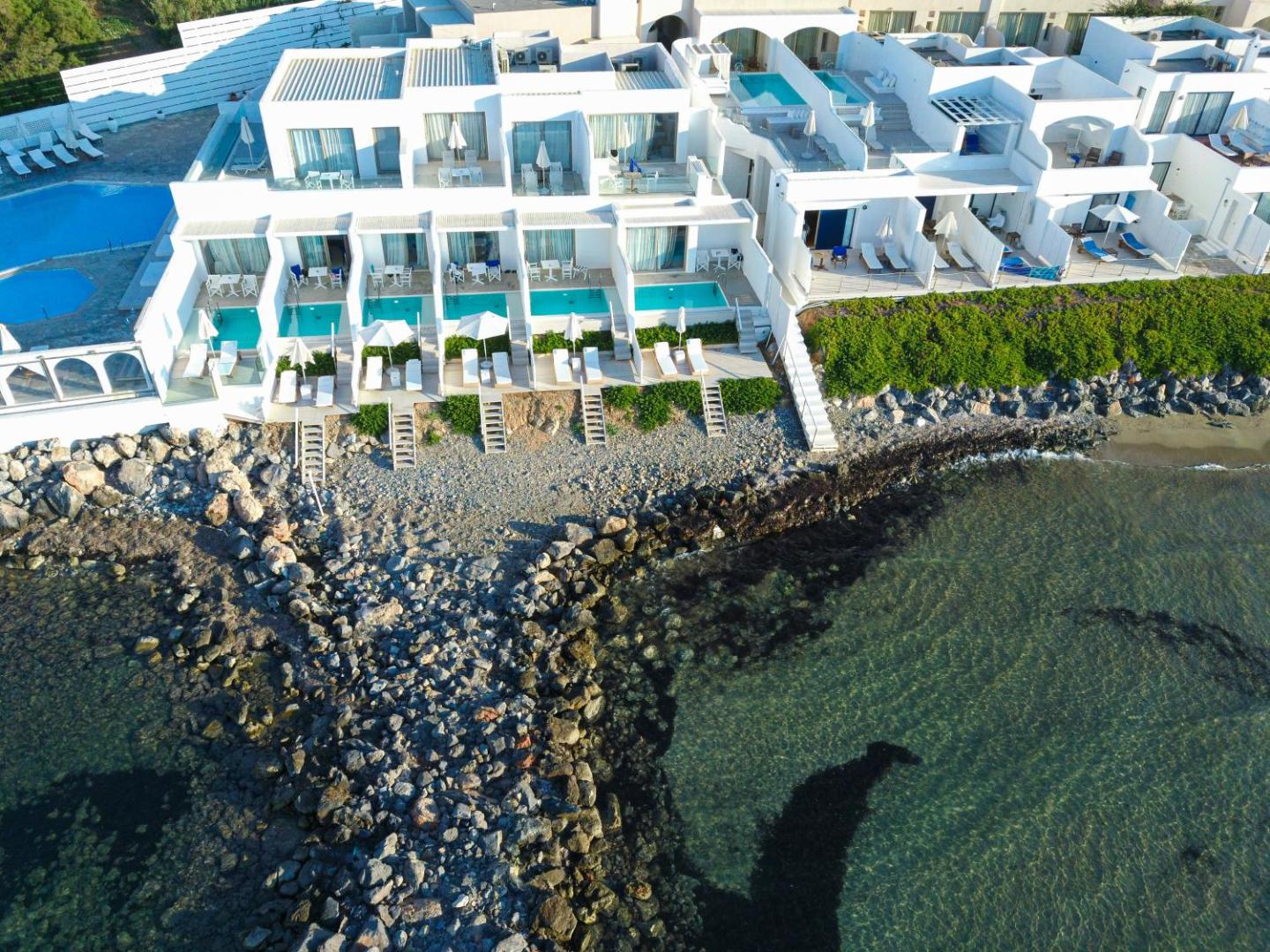 Knossos Beach Bungalows Resort numuri ar privātiem baseiniem un terasēm tieši pie akmeņainās krasta līnijas un dzidrā ūdens