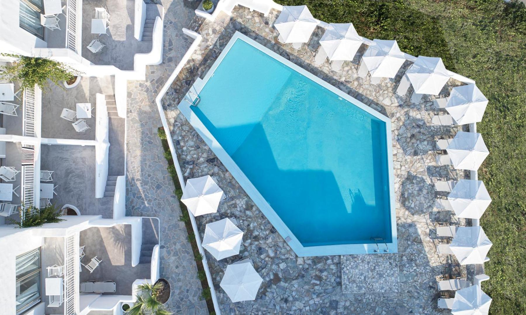 Knossos Beach Bungalows Resort baseina skats no augšas ar saulessargiem un akmens flīžu klājumu Krētas kūrortā