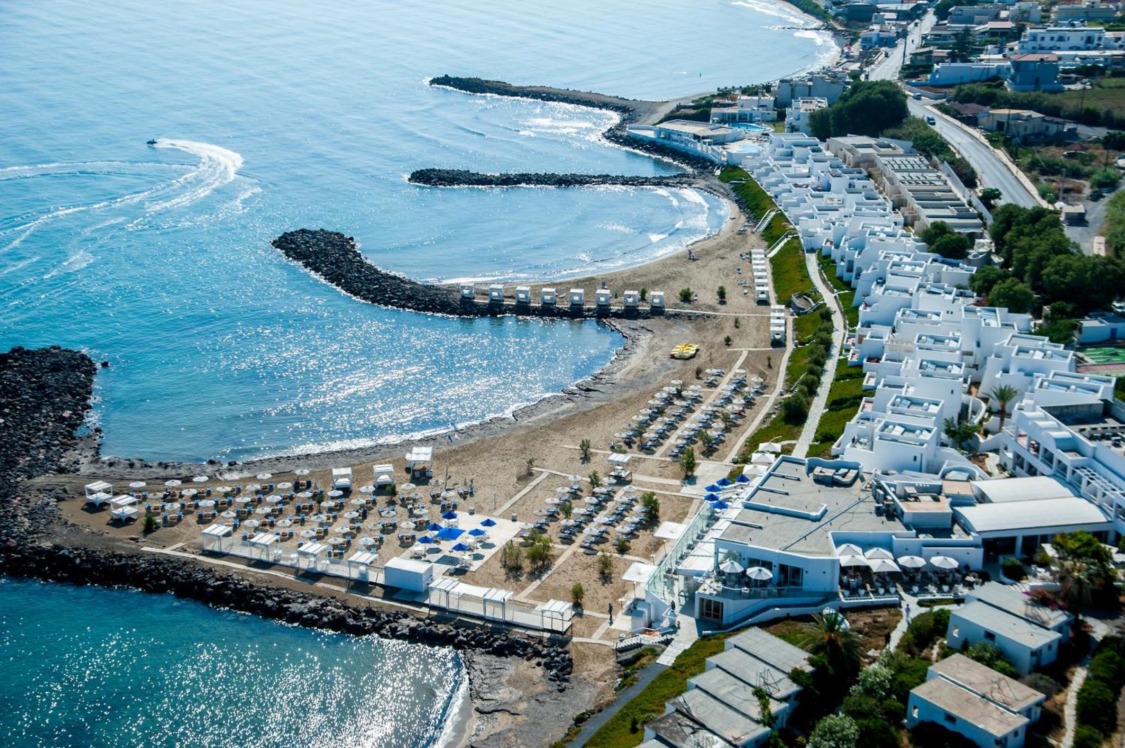 Knossos Beach Bungalows Resort skats no putna lidojuma uz privāto pludmali, saulessargiem un baltajiem bungalo Krētas piekrastē pie Kokini Hani
