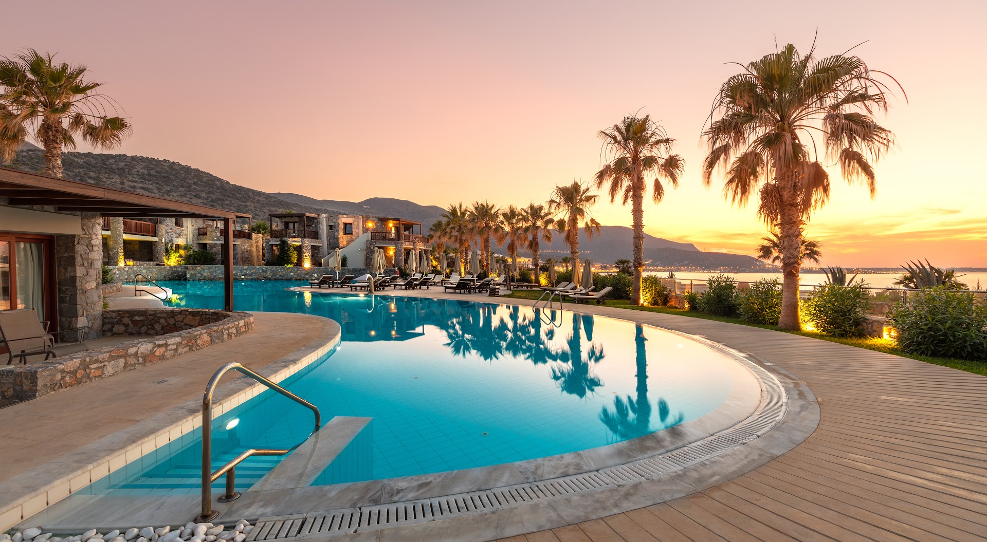 Ikaros Beach Resort & Spa galvenais baseins un palmas saulrietā ar skatu uz kalniem un piekrasti