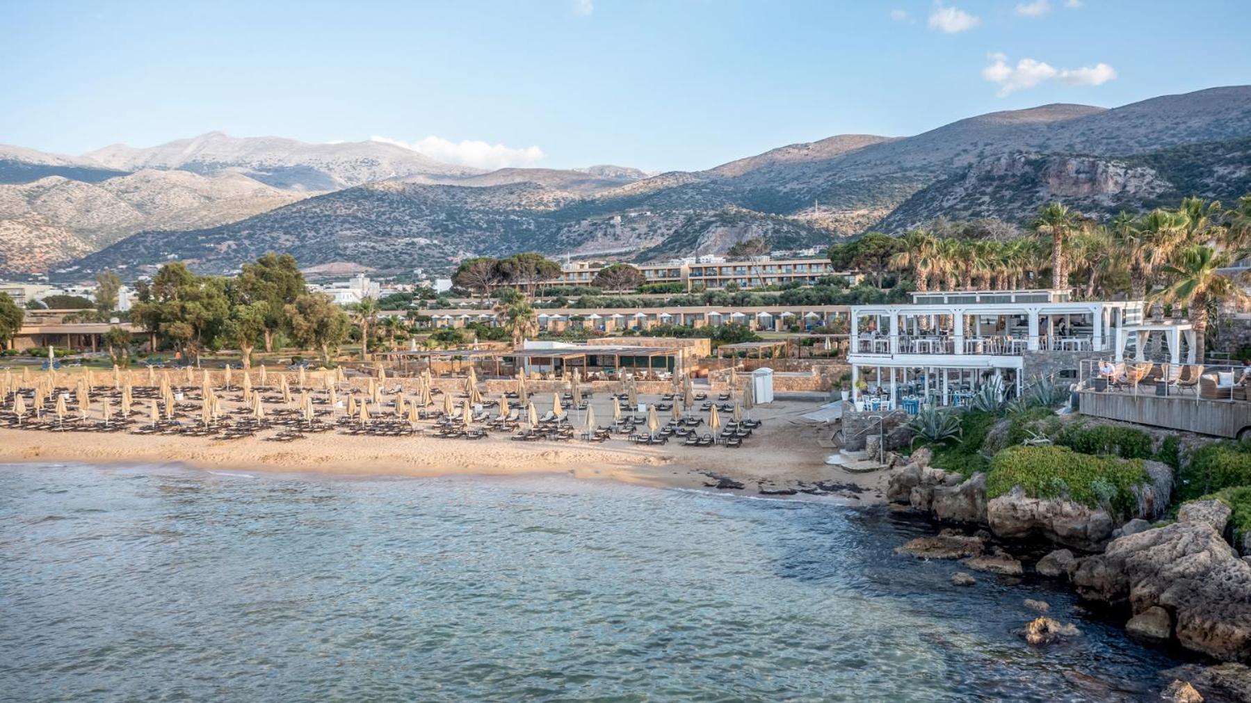 Ikaros Beach Resort & Spa panorāmas skats uz privāto pludmali, viesnīcas ēkām un kalniem fonā Malijas piekrastē