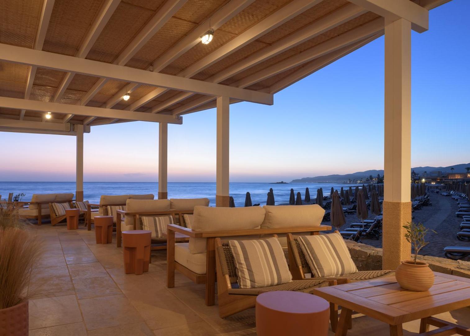 Ikaros Beach Resort & Spa terase ar skatu uz jūru saulrietā — ērti dīvāni un mierpilna atmosfēra piekrastē