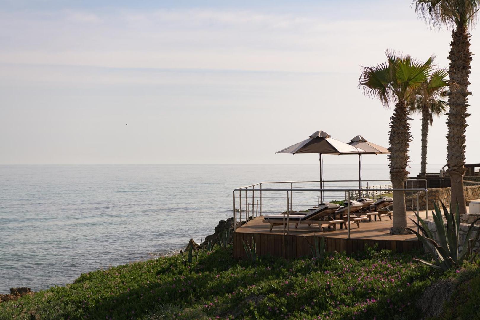 Ikaros Beach Resort & Spa sauļošanās terase uz klints malas ar sauļošanās krēsliem, saulessargiem un skatu uz jūru