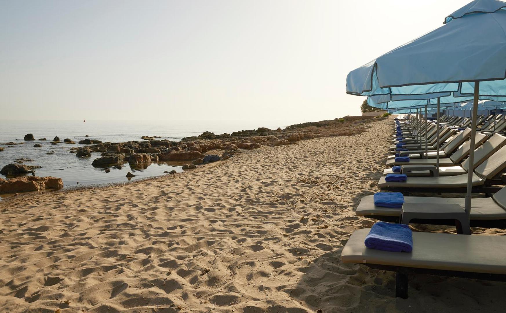 I-Resort Beach Hotel & Spa privātā smilšu pludmale ar sauļošanās krēsliem, saulessargiem un akmeņainu piekrasti Stalidā