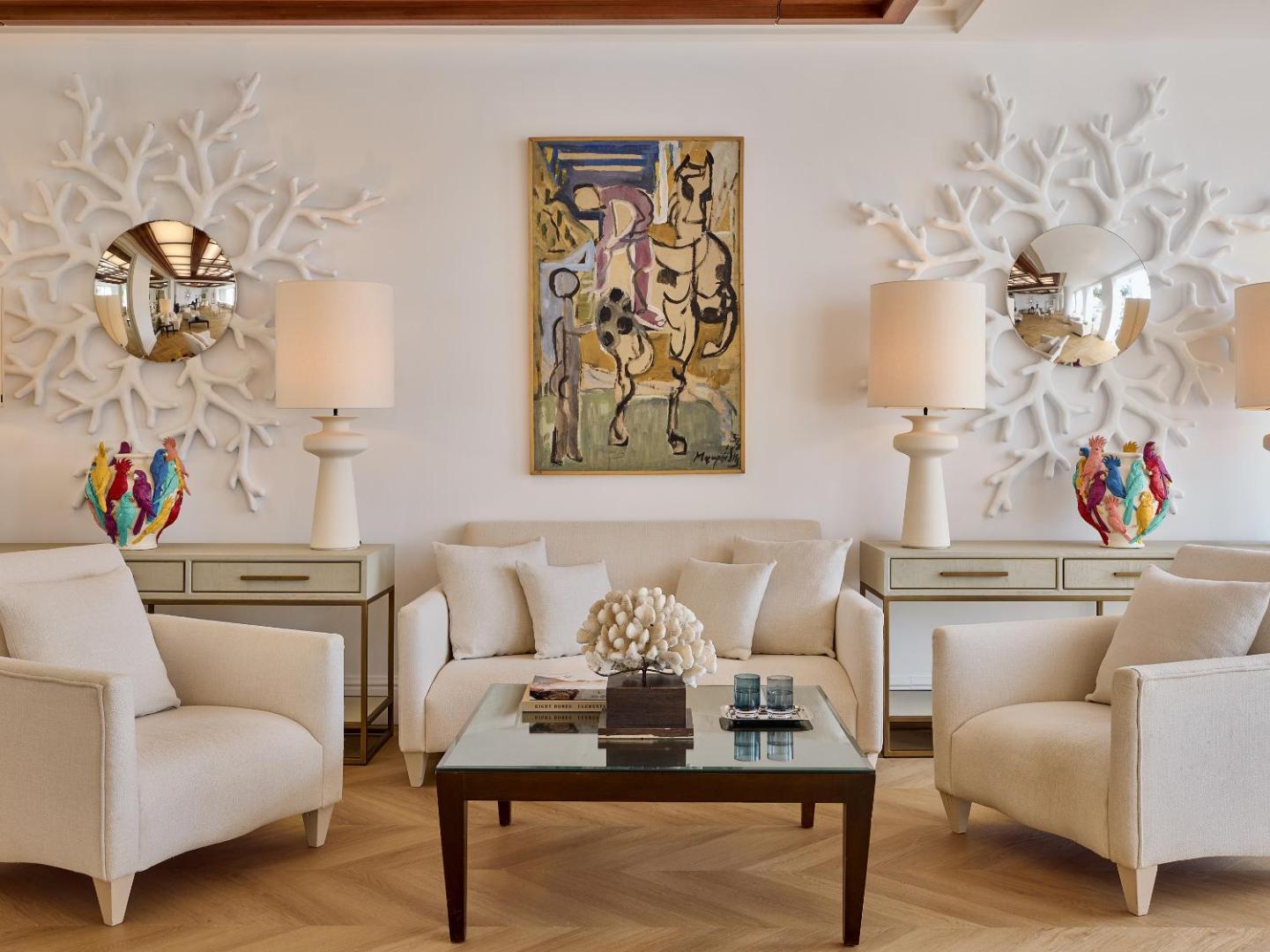 Grecotel Creta Palace Resort eleganta atpūtas zona ar gaišiem dīvāniem, mākslas darbiem un dizaina elementiem viesnīcas lobby interjerā