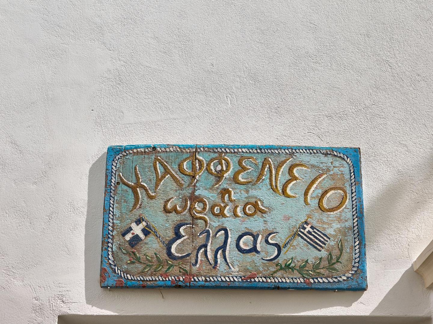 Grecotel Creta Palace tradicionālā grieķu kafenion izkārtne pie baltas sienas — autentiska atmosfēra un vietējā kultūra kūrortā