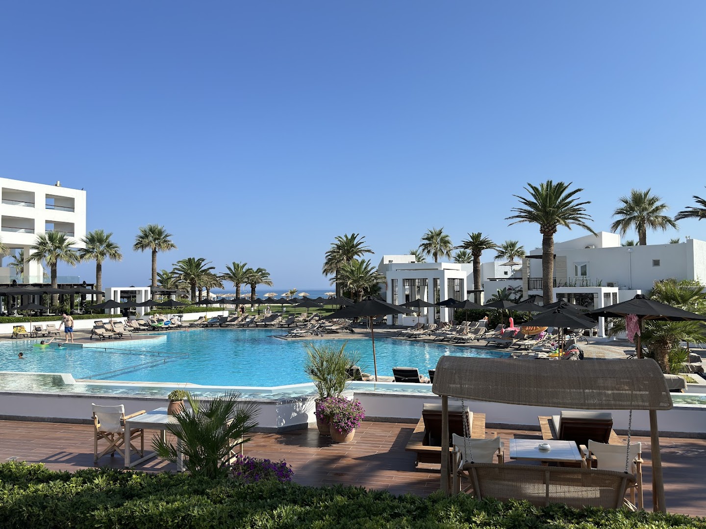Grecotel Creta Palace Resort galvenais baseins ar saulessargiem, atpūtas krēsliem un bāru saulainā pēcpusdienā