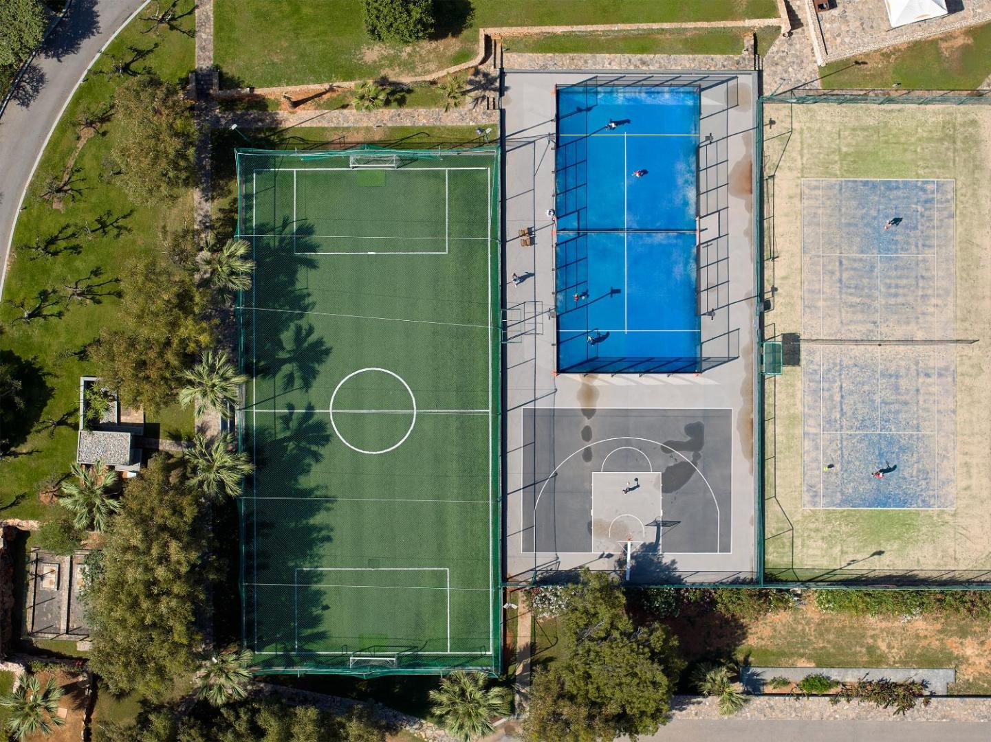 Grecotel Amirandes sporta laukumu skats no augšas — futbola, basketbola, tenisa un padela korti palmu un zaļumu ieskauti