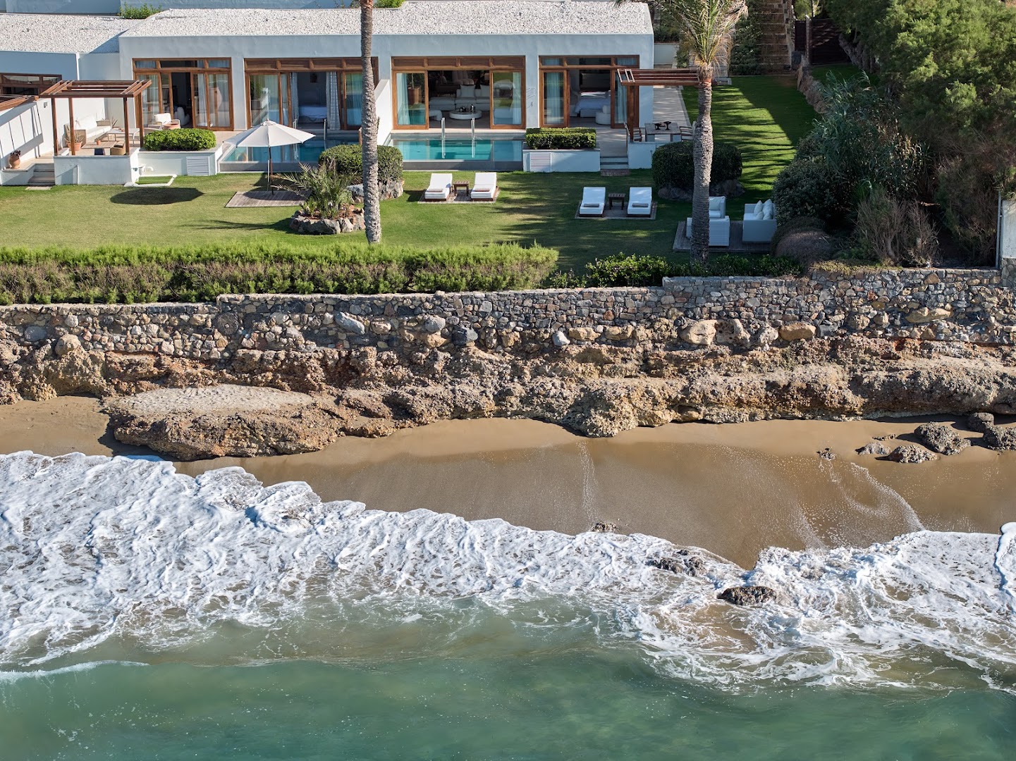 Grecotel Amirandes Exclusive Resort luksusa villas ar privātiem baseiniem piekrastē Krētā — skats no augšas uz dārzu un pludmali