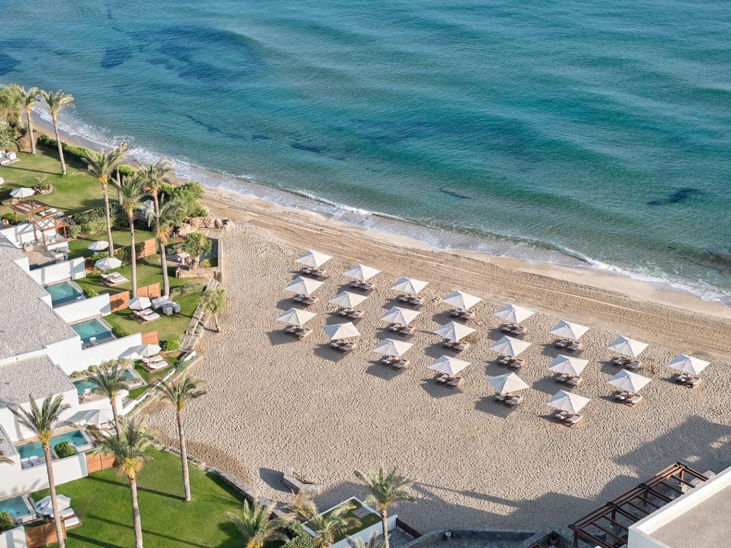 Grecotel Amirandes privātā smilšu pludmale ar saulessargiem un gultām no putna lidojuma skata Krētā
