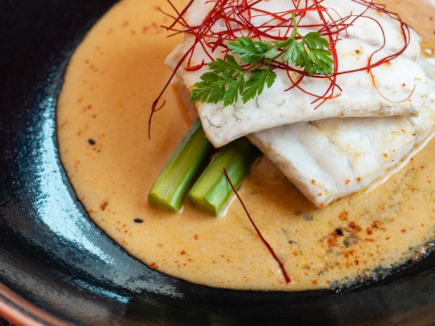 Tuvplāns ar baltas zivs fileju mērcē ar zaļumiem un sparģeļiem Grecotel Amirandes restorānā — augstas klases gastronomija Krētas kūrortā