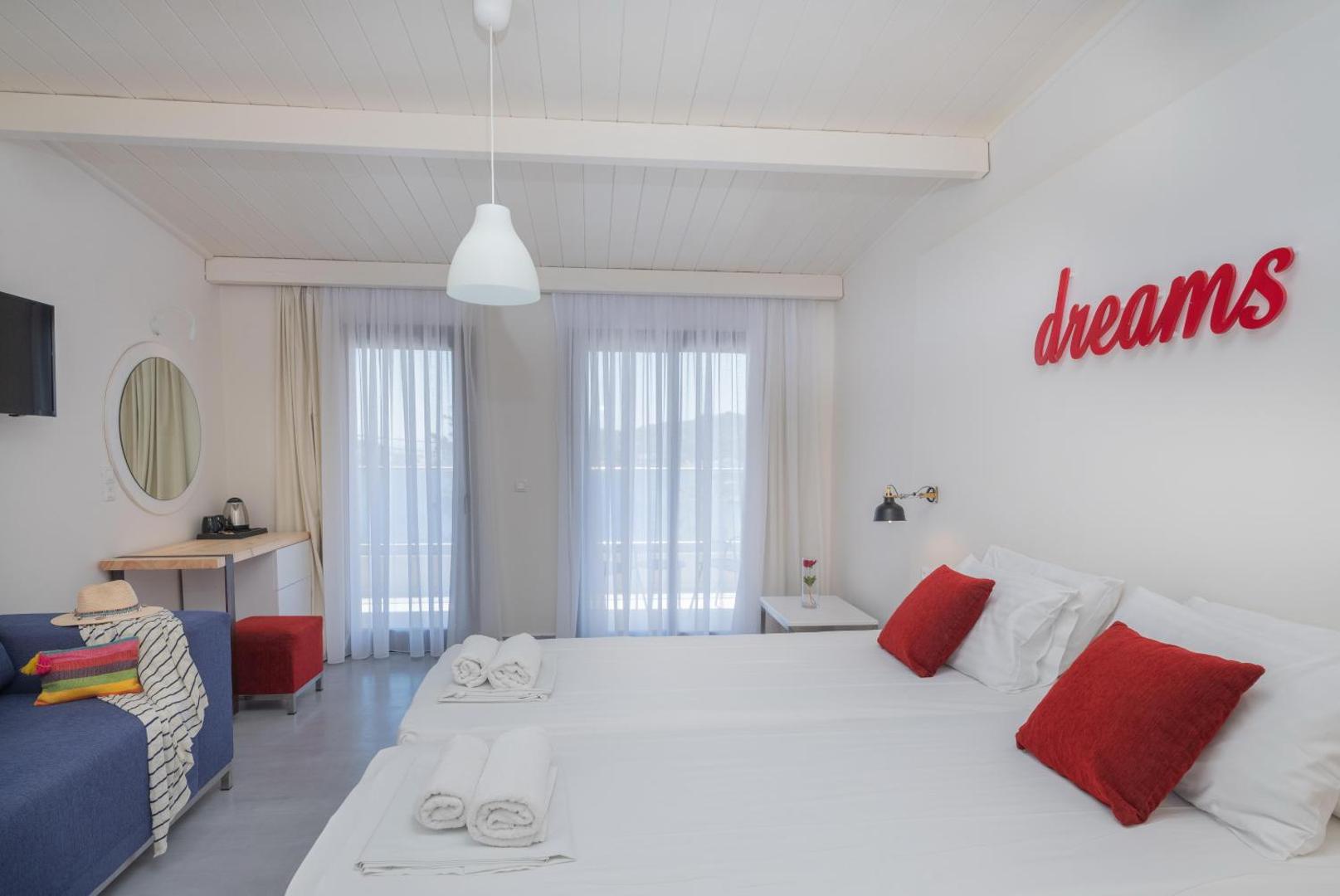 Eva Mare Hotel & Suites gaišs divvietīgs numurs ar balkonu, baltu gultas veļu, sarkaniem dekoratīviem spilveniem un uzrakstu dreams pie sienas