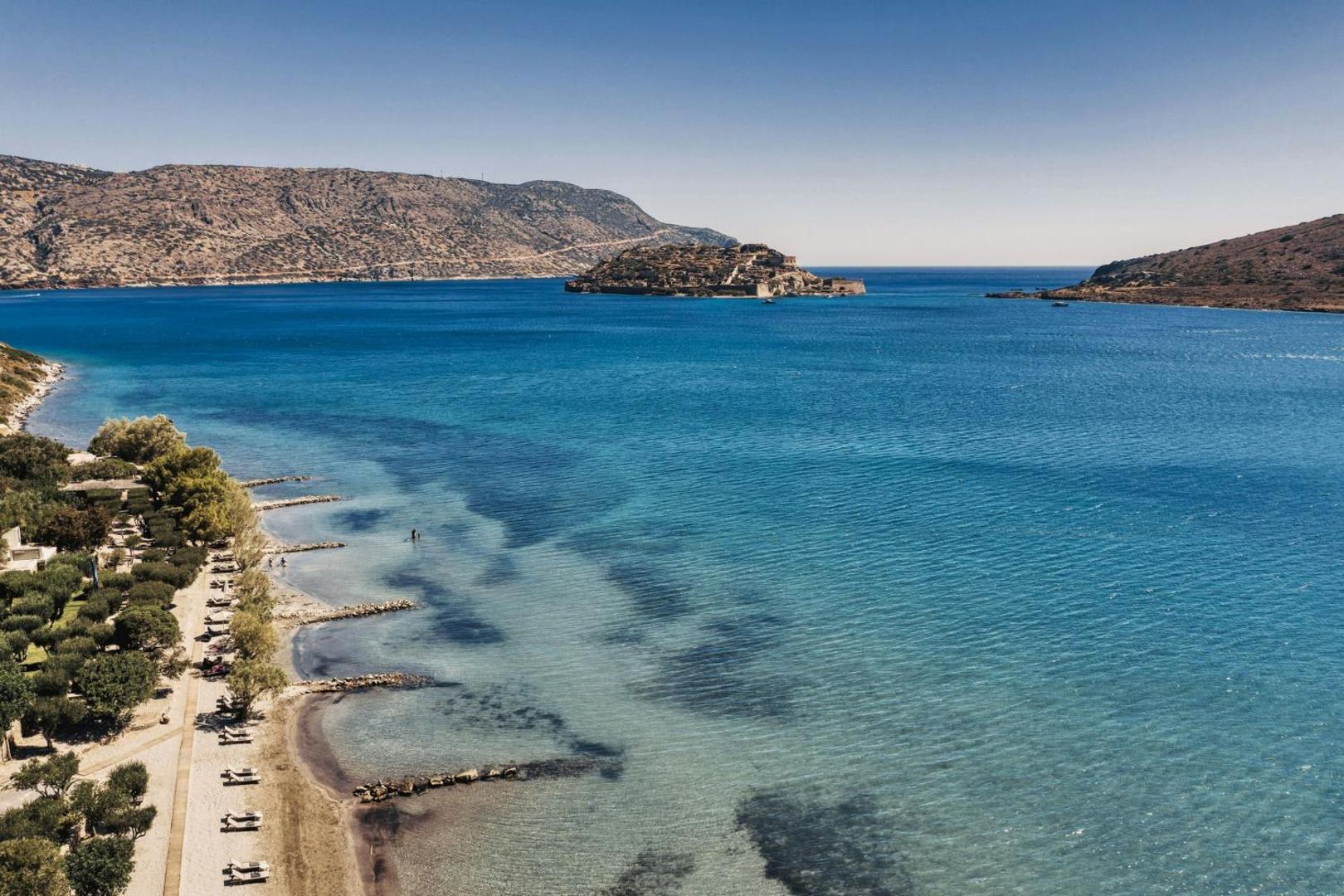 Domes of Elounda viesnīcas panorāmas skats no augšas uz privāto pludmali, dzidro jūru un Spinalongas salu tālumā