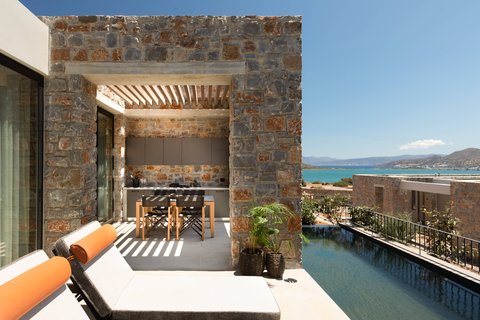 Domes of Elounda Autograph Collection villas terase ar privātu baseinu, sauļošanās krēsliem un āra ēdamzonu pie akmens mūra sienas