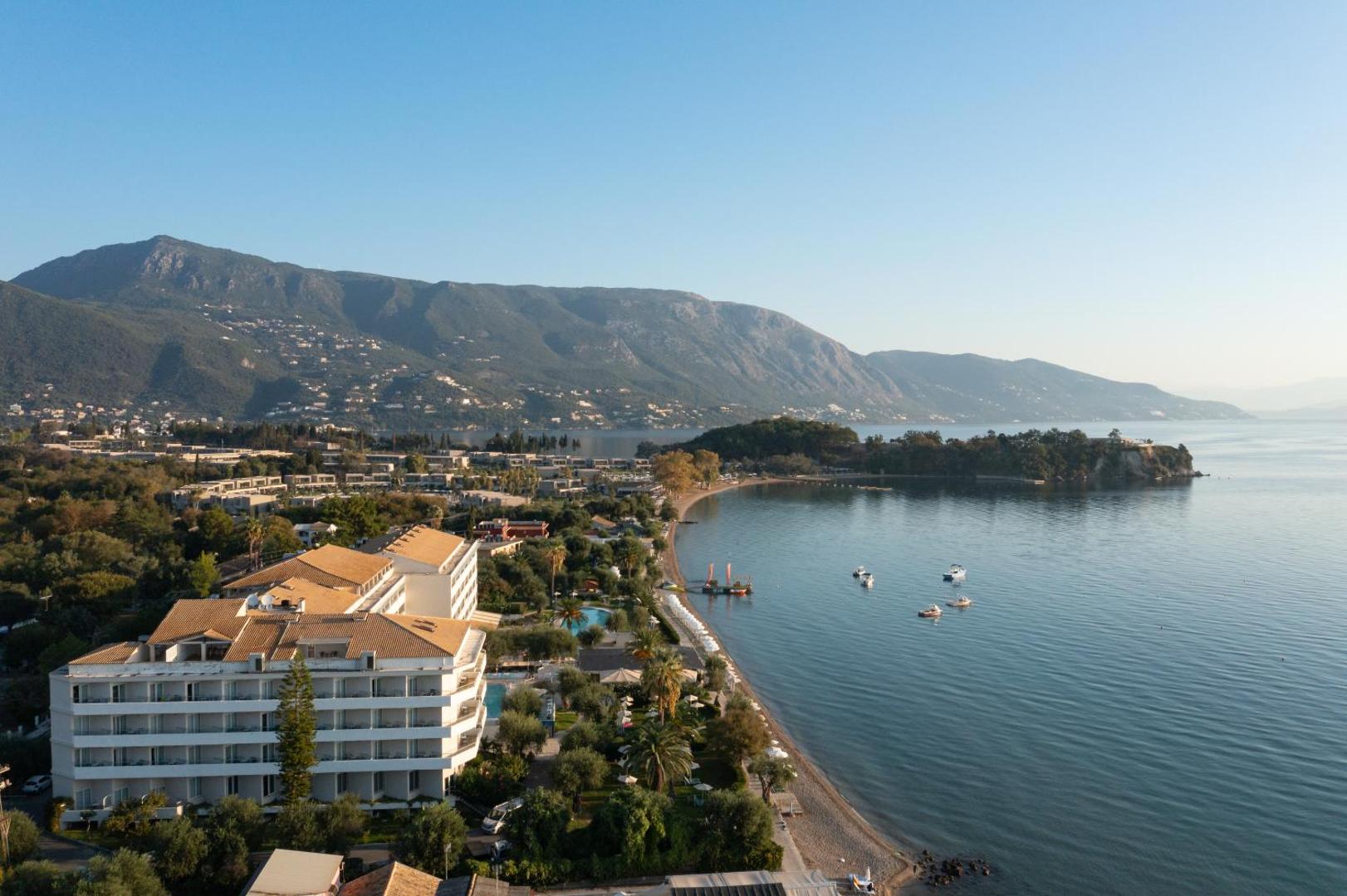 Elea Beach Hotel ēka un piekrastes līnija ar kalniem fonā Dasijā, Korfu — skats uz līci un laivām