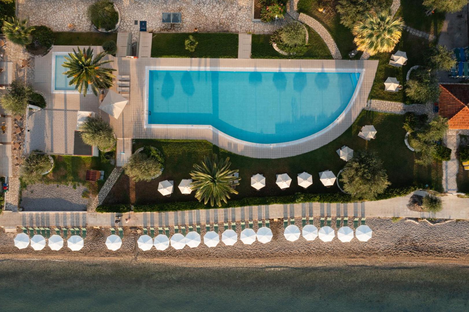 Elea Beach Hotel baseina un pludmales zonas skats no augšas Korfu salā — simetrisks izkārtojums ar saulessargiem un zālienu