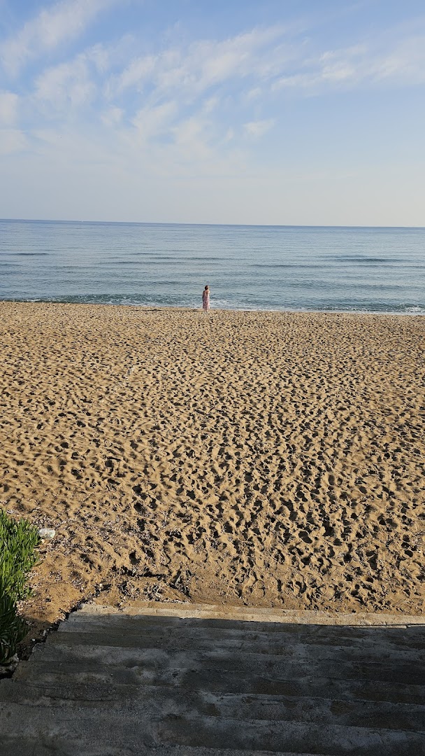 Plaša smilšu pludmale pie Danaos Beach Apartments viesnīcas Krētā ar skatu uz mierīgu jūru un gaišām debesīm