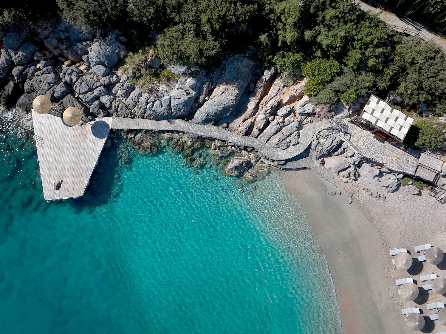 Aerofoto no Daios Cove Luxury Resort pludmales zonas ar koka platformu ūdenī, saulessargiem un dzidru, seklu jūru
