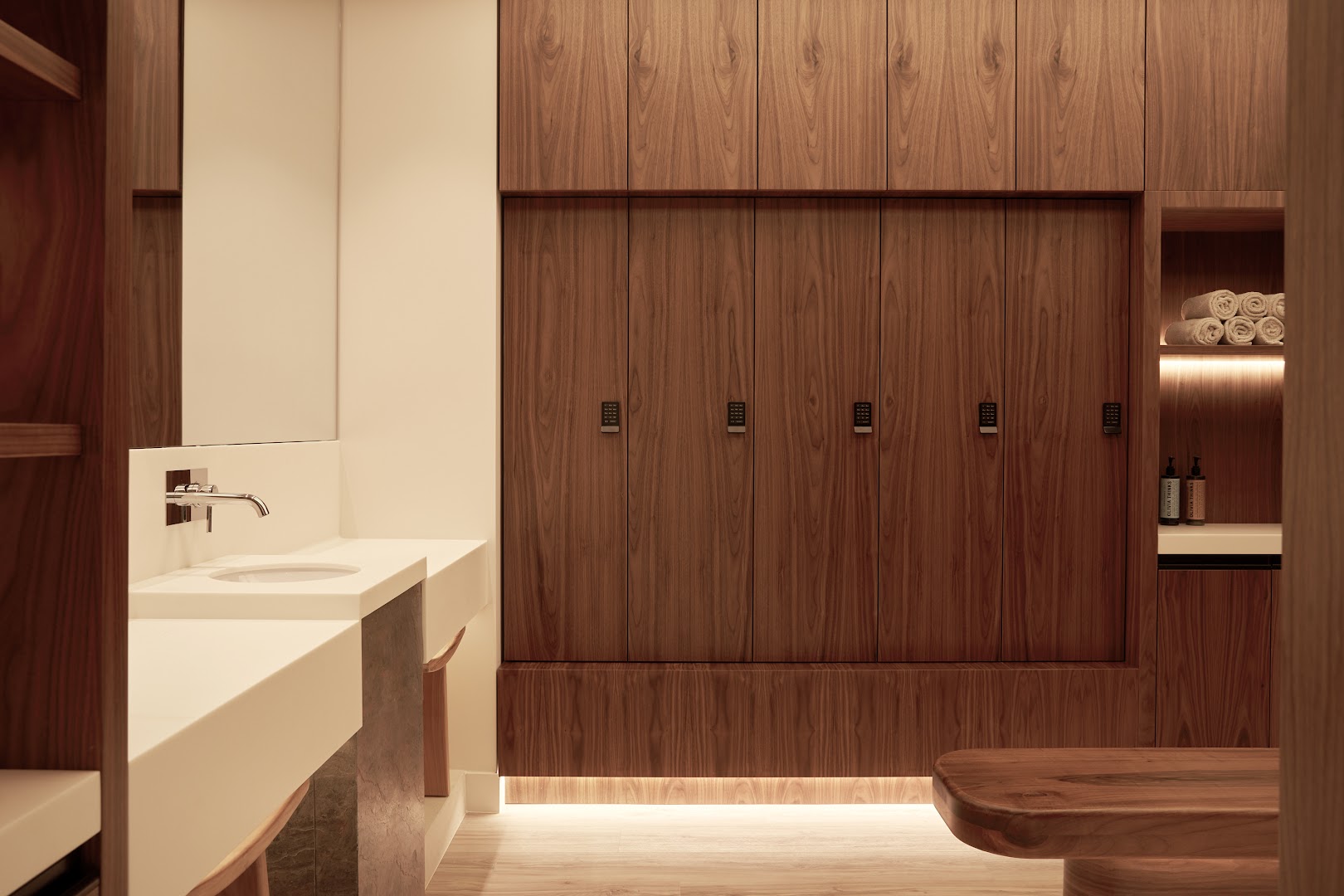 Daios Cove Luxury Resort spa centra ģērbtuve ar koka skapīšiem un modernu izlietni Krētā — elegants interjers ar siltu apgaismojumu