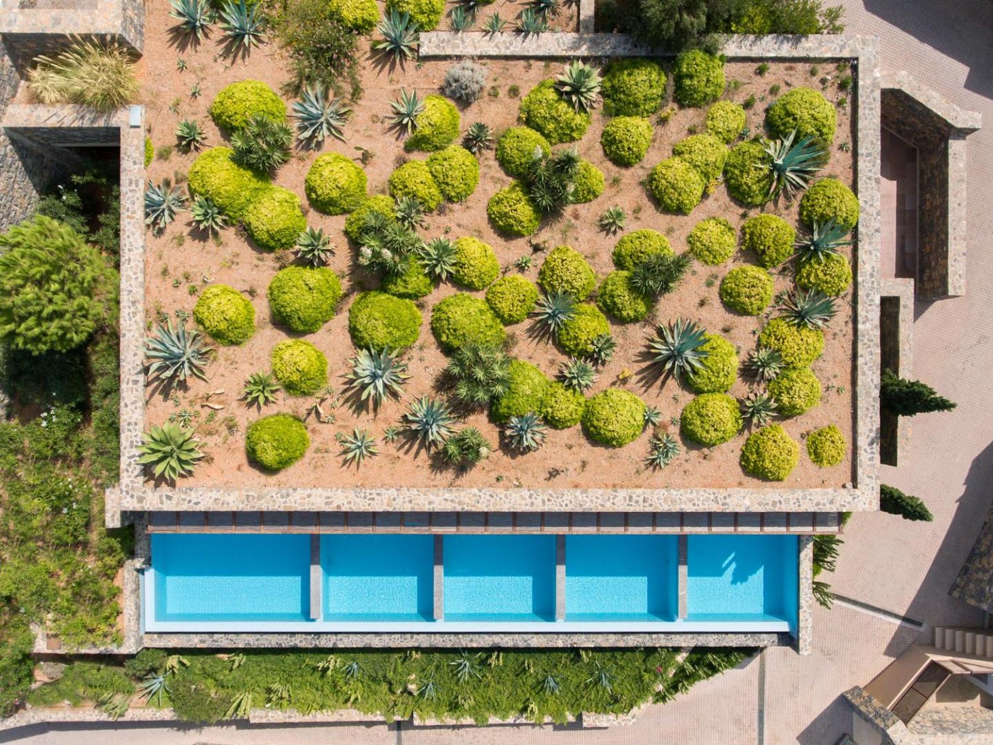 Daios Cove Luxury Resort arhitektūras skats no augšas uz zaļajiem jumtiem un privātajiem baseiniem piekrastes kalnā