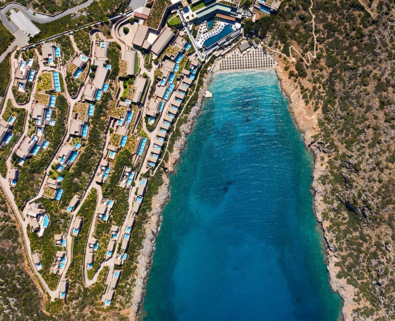 Daios Cove Luxury Resort aerofoto skats no augšas uz kūrorta teritoriju, privāto līci un numuriem ar baseiniem Krētā