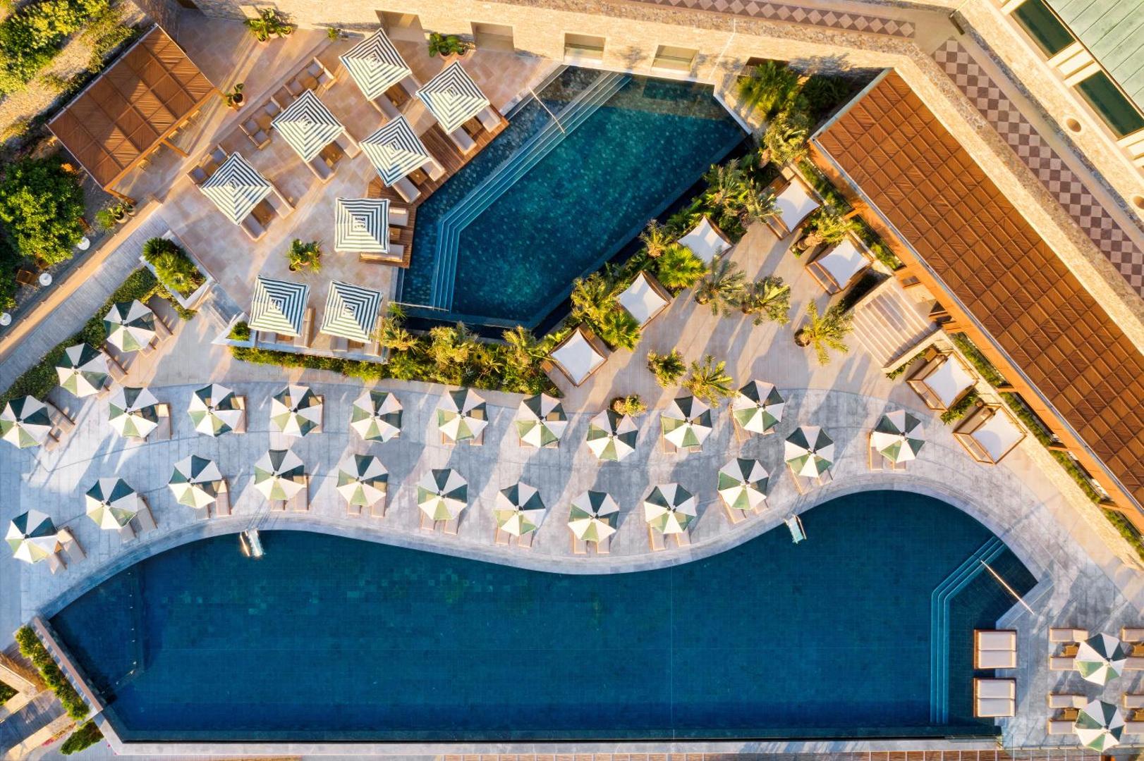 Daios Cove Luxury Resort skats no putna lidojuma uz galveno baseinu zonu ar saulessargiem un atpūtas krēsliem Krētā